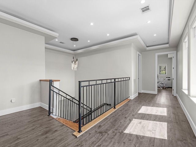 hall featuring ornamental molding, wood-type flooring, and a raised ceiling