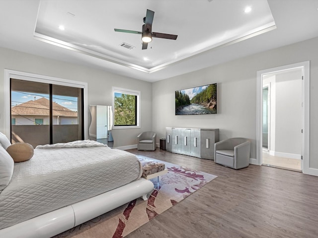 bedroom featuring wood-type flooring, access to outside, ceiling fan, and a tray ceiling