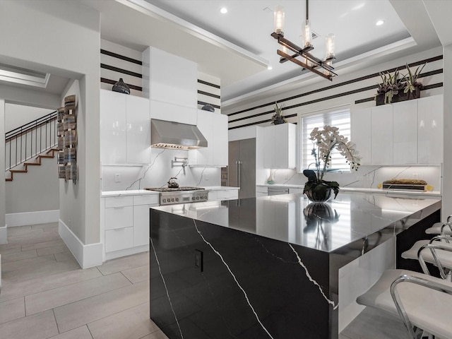 kitchen with decorative light fixtures, dark stone countertops, white cabinets, backsplash, and wall chimney exhaust hood