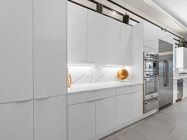 kitchen featuring appliances with stainless steel finishes, white cabinets, light stone counters, and decorative backsplash