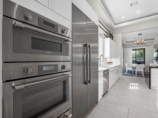 kitchen with light tile patterned flooring, sink, decorative light fixtures, appliances with stainless steel finishes, and a tray ceiling