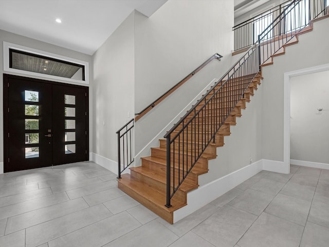 foyer entrance with light tile patterned flooring, a towering ceiling, and french doors