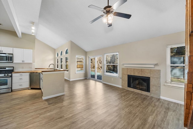 kitchen with vaulted ceiling with beams, white cabinetry, light hardwood / wood-style flooring, appliances with stainless steel finishes, and a fireplace