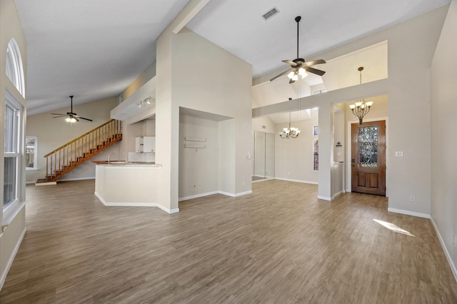 unfurnished living room with ceiling fan with notable chandelier, sink, hardwood / wood-style floors, and high vaulted ceiling