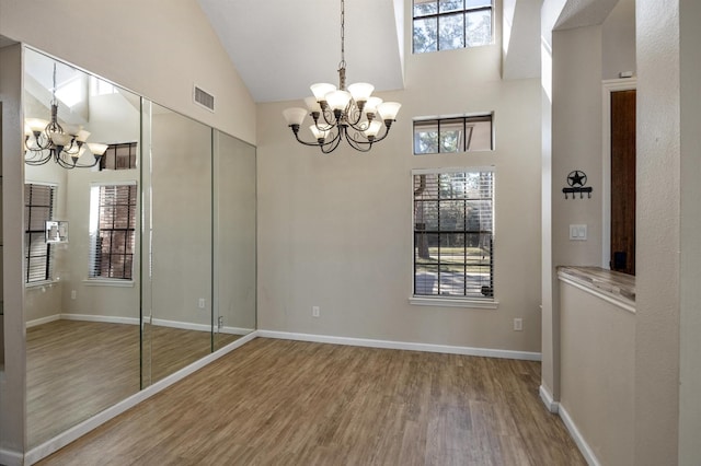 unfurnished dining area with high vaulted ceiling, hardwood / wood-style floors, and a chandelier