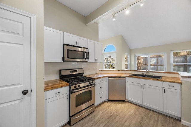 kitchen with sink, butcher block countertops, vaulted ceiling with beams, stainless steel appliances, and white cabinets