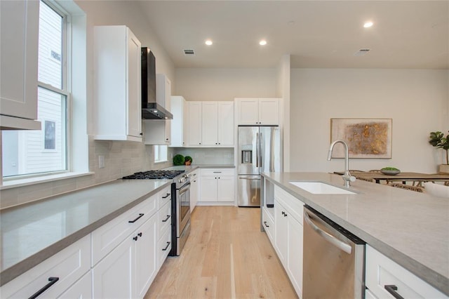 kitchen featuring sink, white cabinetry, light wood-type flooring, appliances with stainless steel finishes, and wall chimney range hood