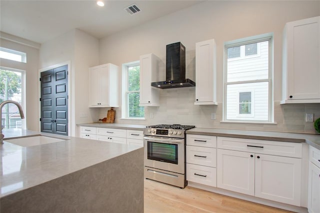 kitchen featuring wall chimney exhaust hood, sink, white cabinetry, stainless steel range with gas cooktop, and decorative backsplash