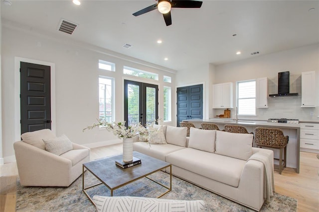 living room with french doors, ceiling fan, sink, and light hardwood / wood-style flooring