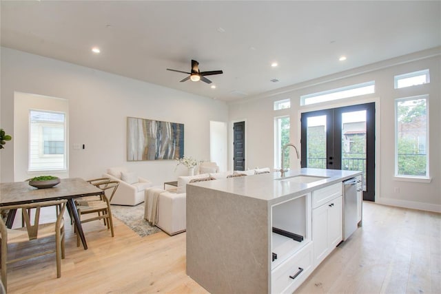 kitchen with french doors, sink, white cabinetry, light hardwood / wood-style flooring, and a kitchen island with sink