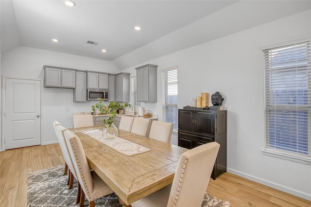 dining area with sink, vaulted ceiling, and light hardwood / wood-style flooring