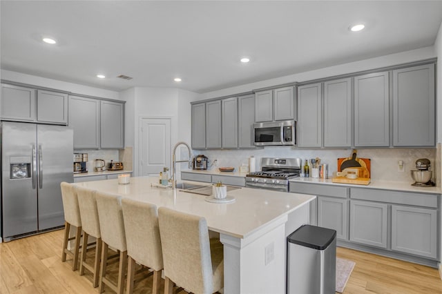 kitchen featuring stainless steel appliances, gray cabinets, a kitchen island with sink, and a breakfast bar area