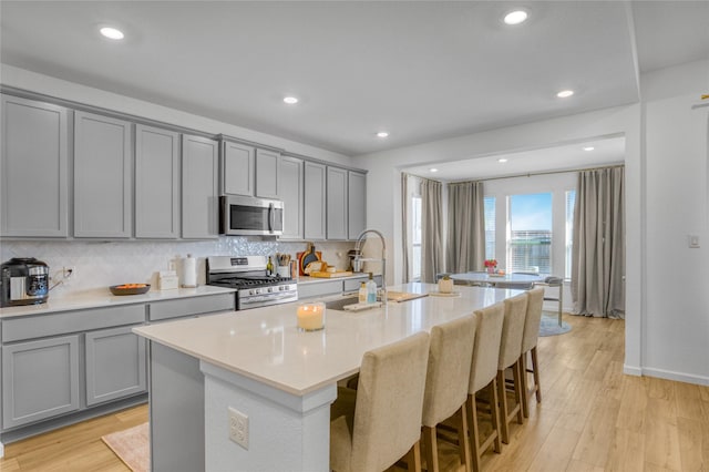 kitchen with appliances with stainless steel finishes, a breakfast bar area, a center island with sink, and gray cabinetry