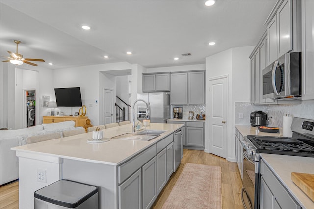 kitchen with stainless steel appliances, an island with sink, and light hardwood / wood-style floors