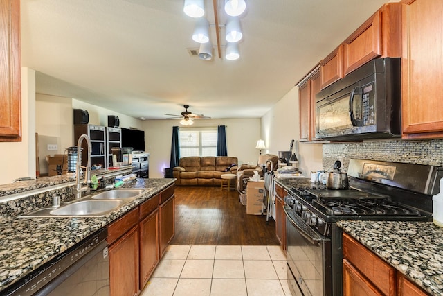 kitchen with sink, light tile patterned floors, dark stone countertops, black appliances, and decorative backsplash