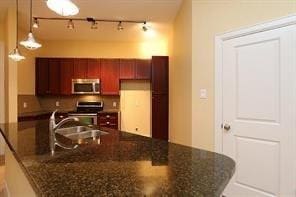 kitchen with pendant lighting, stainless steel appliances, sink, and dark stone countertops