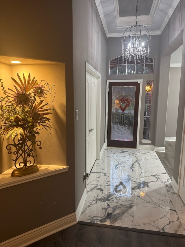 foyer entrance featuring a raised ceiling, ornamental molding, and a notable chandelier