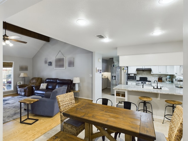 dining room featuring vaulted ceiling with beams, light hardwood / wood-style floors, sink, and ceiling fan