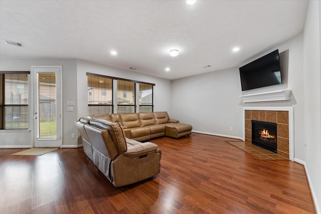 living area featuring a tile fireplace, dark wood finished floors, visible vents, and baseboards