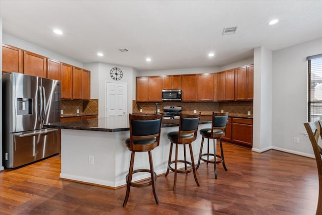 kitchen featuring a breakfast bar area, stainless steel appliances, dark wood-style flooring, a kitchen island, and visible vents