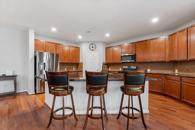 kitchen with visible vents, stainless steel appliances, a kitchen island with sink, and a kitchen breakfast bar