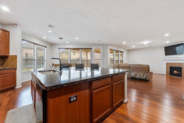 kitchen with a sink, open floor plan, dishwasher, an island with sink, and dark stone countertops