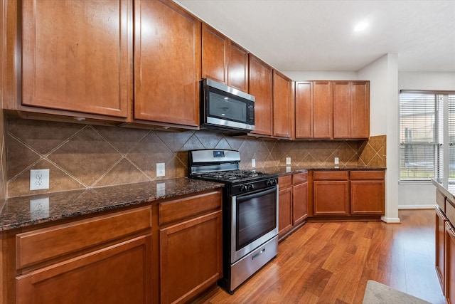 kitchen featuring light wood-style flooring, appliances with stainless steel finishes, brown cabinets, and dark stone countertops