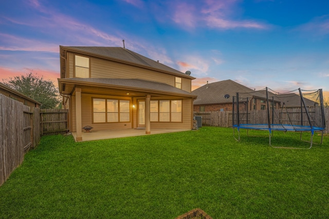 back of house with a trampoline, a patio area, a fenced backyard, and a lawn