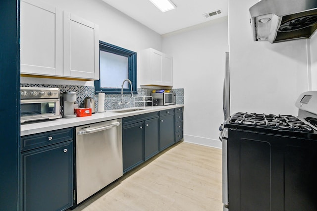 kitchen with appliances with stainless steel finishes, sink, white cabinets, decorative backsplash, and exhaust hood