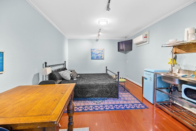 bedroom featuring hardwood / wood-style flooring, ornamental molding, rail lighting, and a wall unit AC