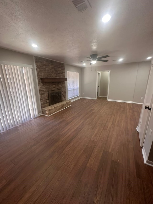 unfurnished living room with visible vents, a textured ceiling, a brick fireplace, and dark wood finished floors