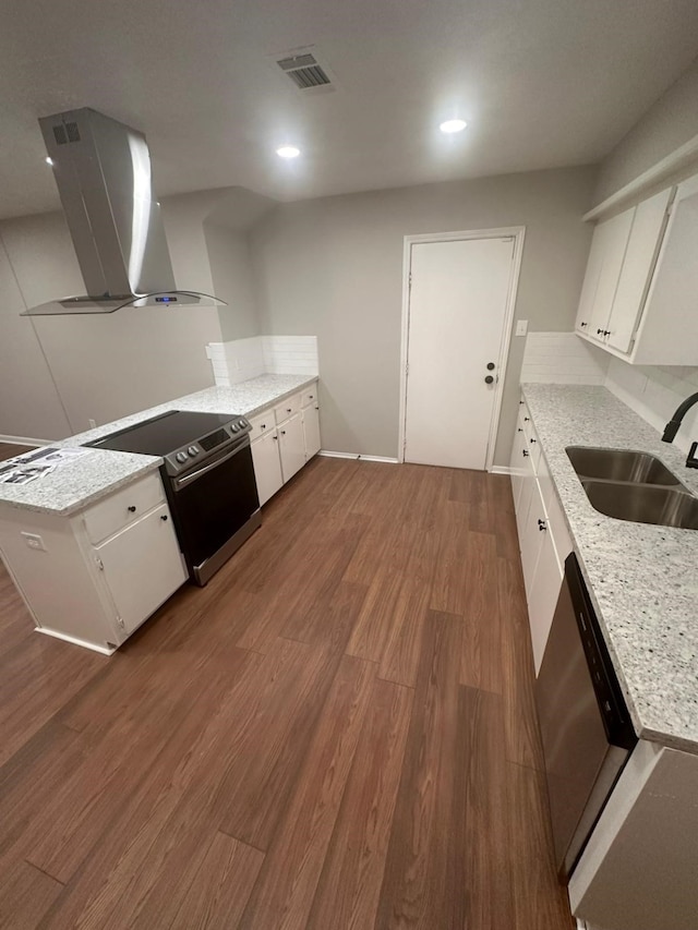 kitchen with dark wood-type flooring, wall chimney range hood, appliances with stainless steel finishes, a peninsula, and a sink