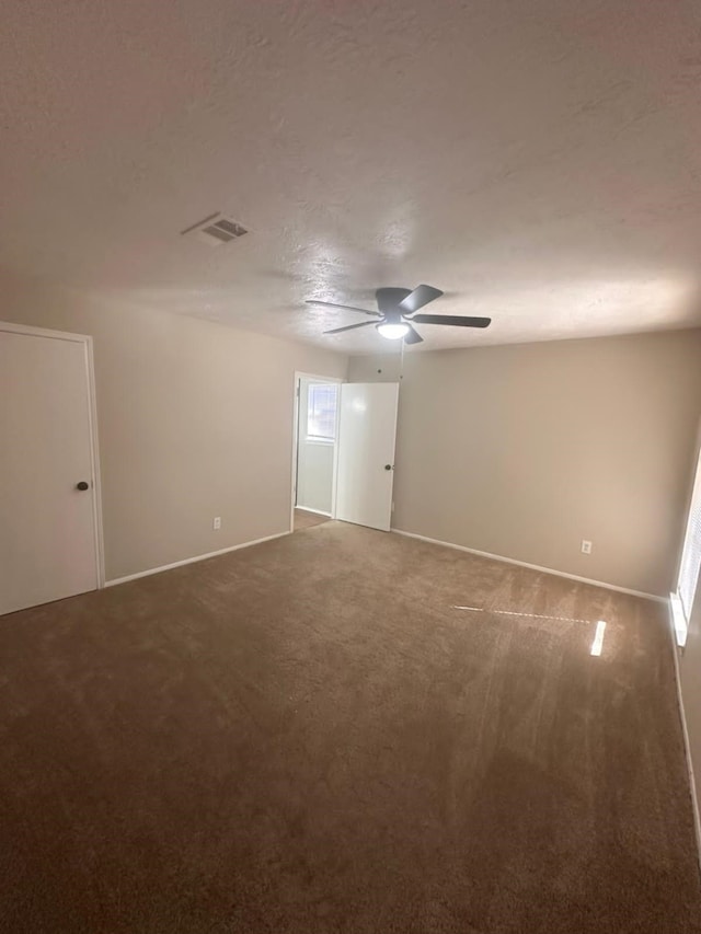 spare room with carpet, baseboards, visible vents, ceiling fan, and a textured ceiling