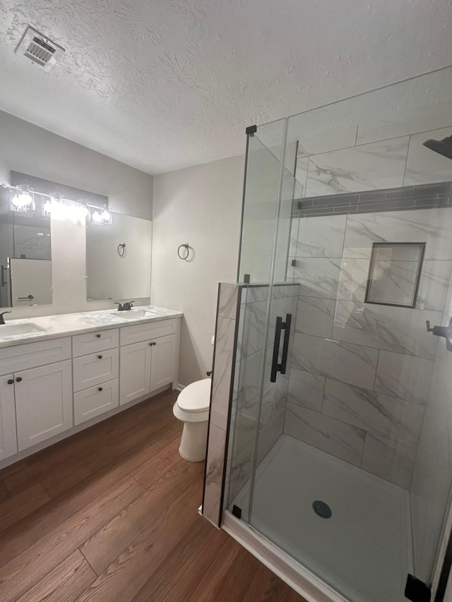 bathroom with hardwood / wood-style flooring, vanity, an enclosed shower, toilet, and a textured ceiling