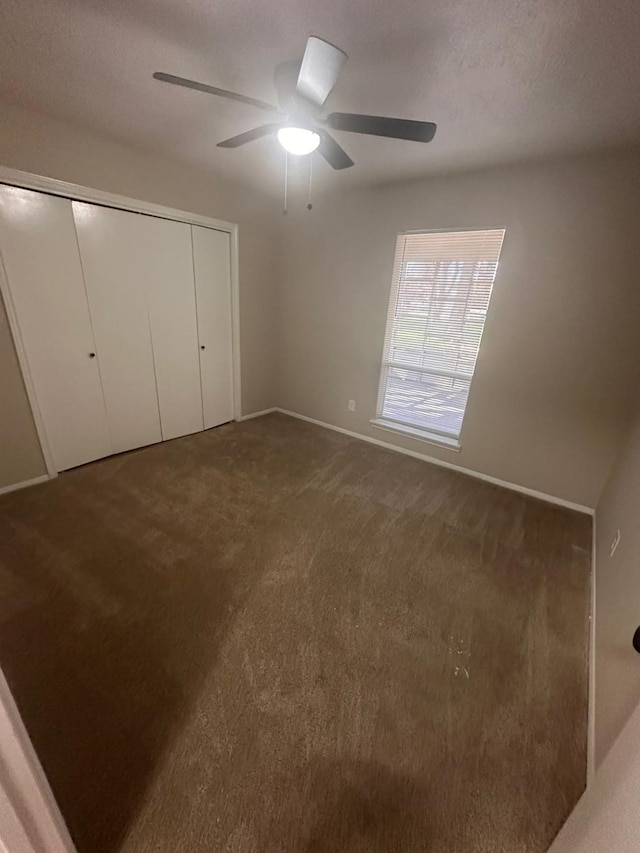 unfurnished bedroom with ceiling fan, dark carpet, a closet, and a textured ceiling