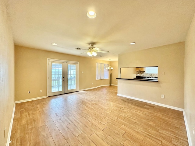 unfurnished living room featuring ceiling fan with notable chandelier, light hardwood / wood-style floors, and french doors