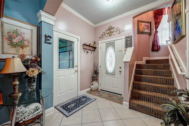 entryway featuring a textured ceiling, light tile patterned flooring, ornamental molding, stairway, and decorative columns