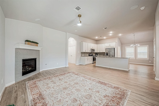 living room with ceiling fan with notable chandelier, lofted ceiling, sink, a brick fireplace, and light hardwood / wood-style flooring