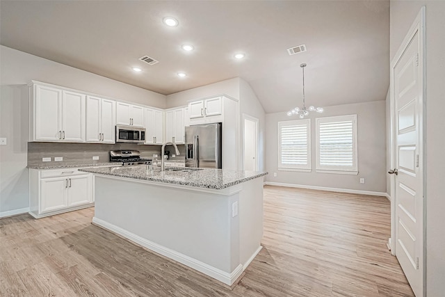 kitchen with white cabinetry, a center island with sink, appliances with stainless steel finishes, light stone countertops, and light hardwood / wood-style floors