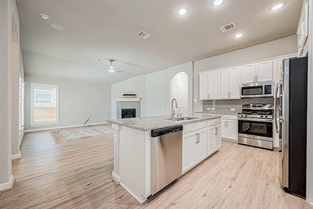 kitchen featuring light hardwood / wood-style flooring, appliances with stainless steel finishes, white cabinetry, light stone counters, and an island with sink