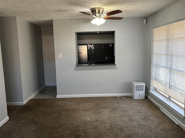 empty room with ceiling fan, a textured ceiling, and dark carpet