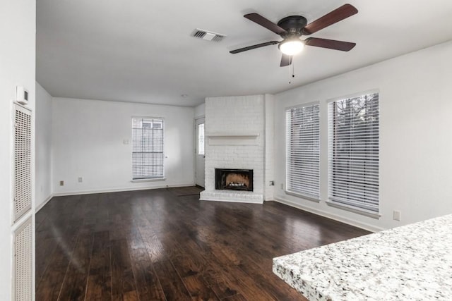 unfurnished living room with ceiling fan, dark hardwood / wood-style flooring, and a brick fireplace