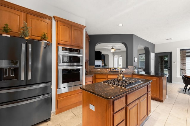 kitchen with stainless steel appliances, dark stone counters, a kitchen island, and light tile patterned floors