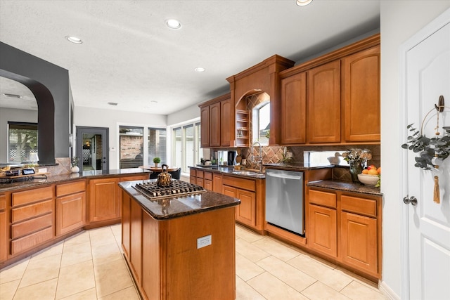 kitchen featuring light tile patterned floors, backsplash, stainless steel appliances, a kitchen island, and dark stone counters