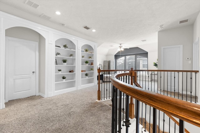 hallway with built in features, light colored carpet, and a textured ceiling