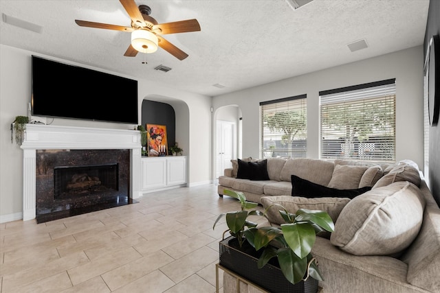 living room featuring a premium fireplace, a textured ceiling, and ceiling fan