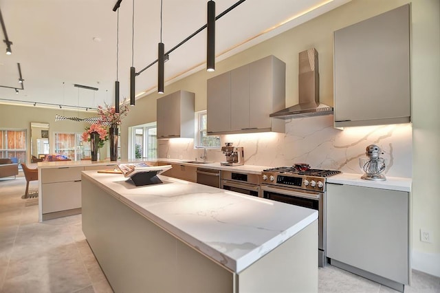 kitchen featuring gray cabinetry, appliances with stainless steel finishes, kitchen peninsula, pendant lighting, and wall chimney range hood