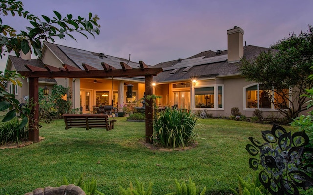 back house at dusk featuring outdoor lounge area, a lawn, ceiling fan, and solar panels