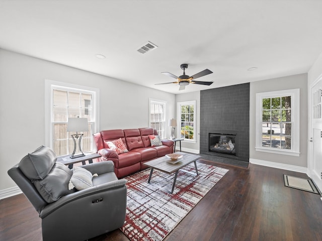 living room with a healthy amount of sunlight, a brick fireplace, dark wood-type flooring, and ceiling fan