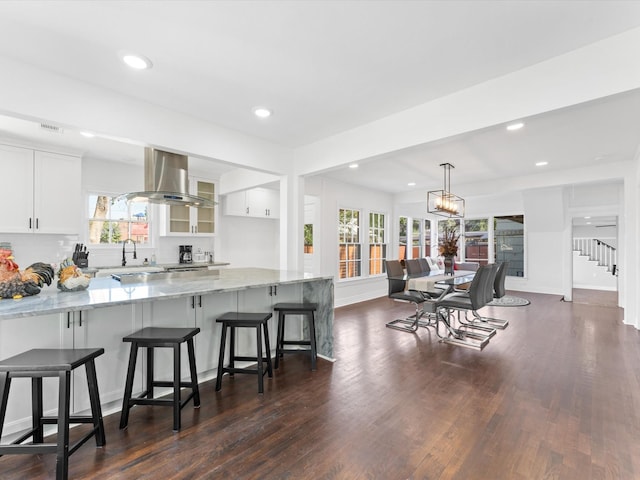 kitchen featuring white cabinetry, light stone counters, a kitchen breakfast bar, dark hardwood / wood-style flooring, and island exhaust hood